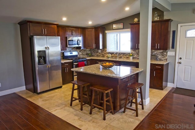 kitchen with lofted ceiling, a breakfast bar area, stainless steel appliances, a center island, and light stone countertops