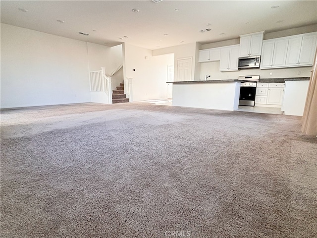 kitchen with stainless steel appliances, light carpet, white cabinetry, dark countertops, and open floor plan