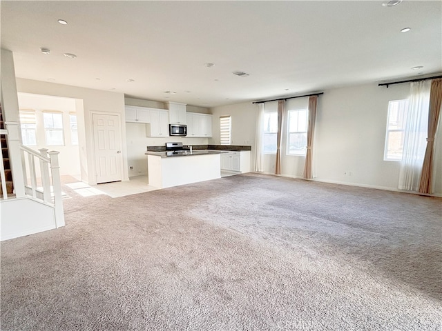 interior space with dark countertops, open floor plan, white cabinetry, stainless steel appliances, and light colored carpet