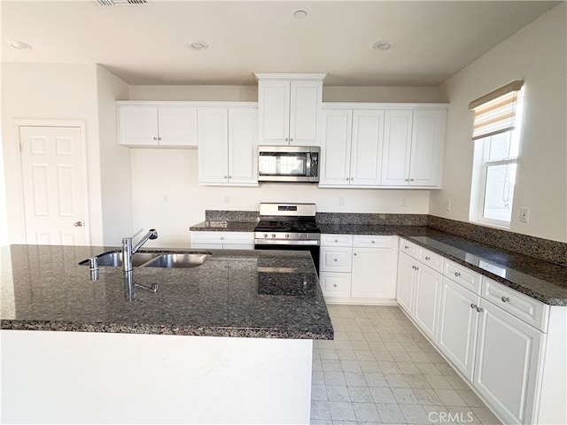 kitchen featuring a sink, dark stone counters, white cabinetry, and stainless steel appliances