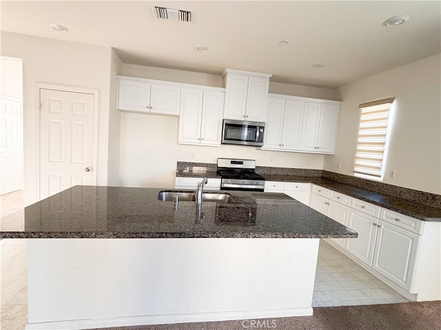 kitchen featuring visible vents, a center island with sink, white cabinets, stainless steel appliances, and a sink