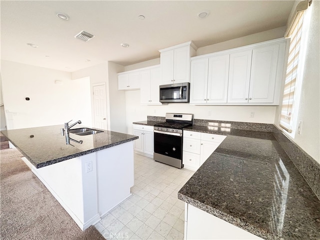 kitchen featuring visible vents, a center island with sink, a sink, white cabinetry, and appliances with stainless steel finishes