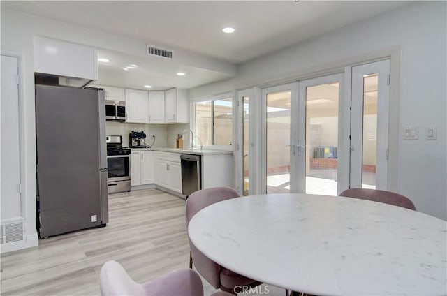 kitchen featuring light hardwood / wood-style flooring, stainless steel appliances, white cabinets, decorative backsplash, and french doors