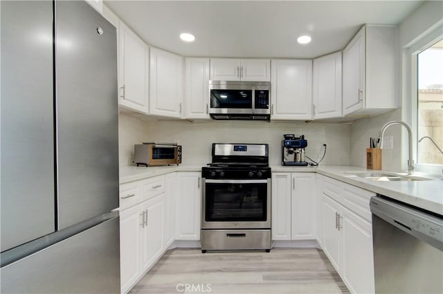 kitchen with appliances with stainless steel finishes, sink, white cabinets, and light wood-type flooring