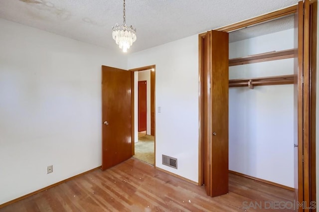 unfurnished bedroom with an inviting chandelier, hardwood / wood-style floors, a closet, and a textured ceiling