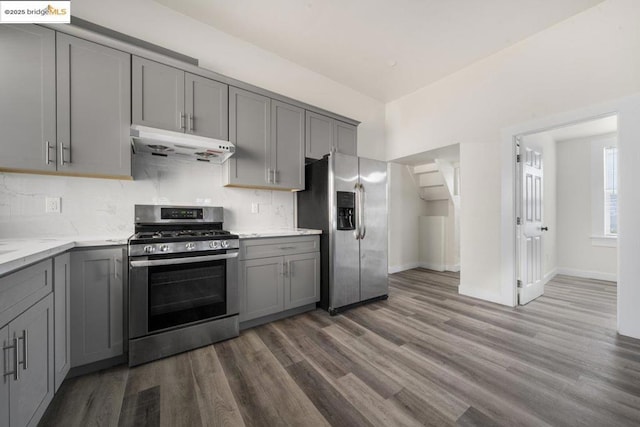 kitchen featuring appliances with stainless steel finishes, gray cabinetry, dark hardwood / wood-style flooring, decorative backsplash, and light stone counters