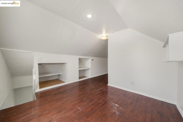 additional living space with dark hardwood / wood-style flooring, vaulted ceiling, and built in features