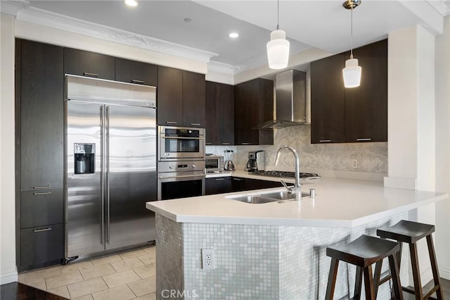 kitchen with appliances with stainless steel finishes, a breakfast bar, decorative light fixtures, kitchen peninsula, and wall chimney range hood