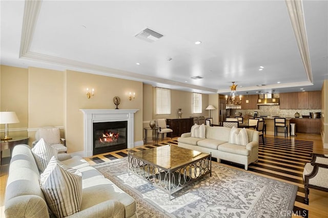 living room with crown molding, light hardwood / wood-style flooring, a chandelier, and a tray ceiling