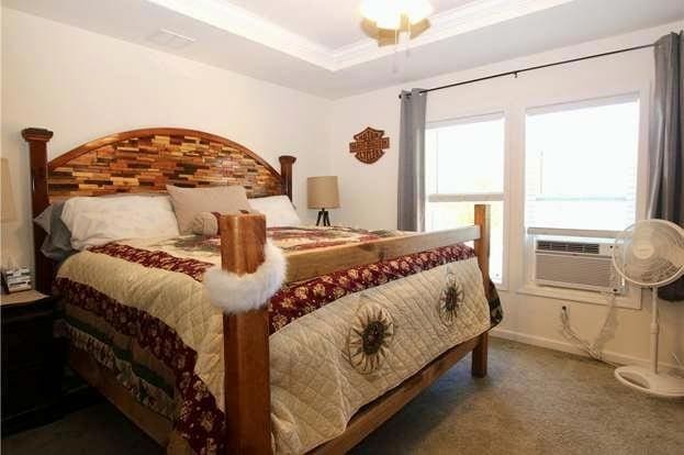 carpeted bedroom featuring multiple windows, cooling unit, and a tray ceiling