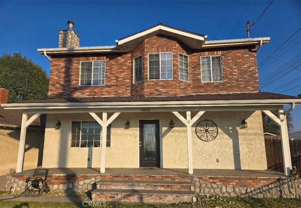 exterior space featuring a porch, brick siding, and a chimney