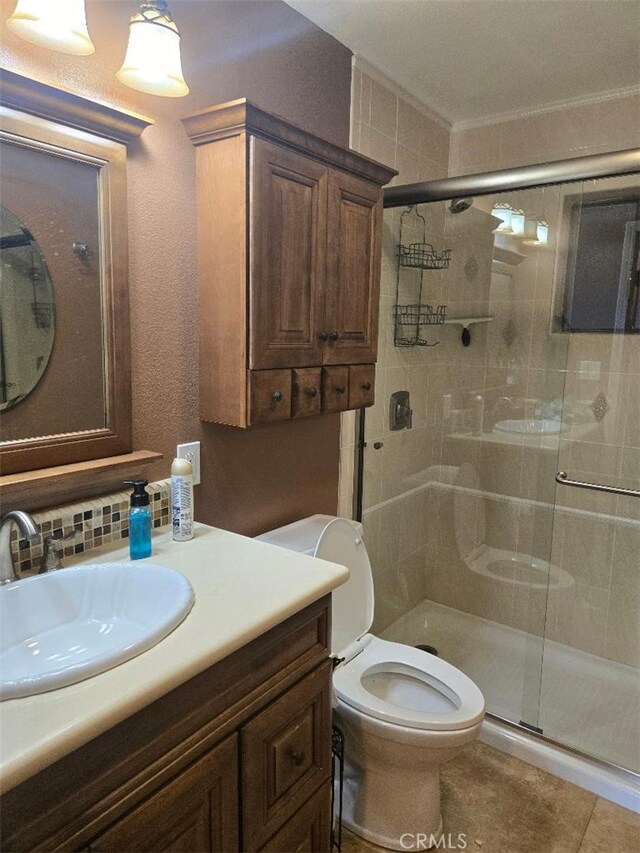 bathroom with tile patterned floors, toilet, a shower with shower door, vanity, and ornamental molding