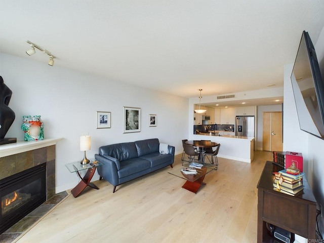 living room with a tiled fireplace, track lighting, and light hardwood / wood-style floors