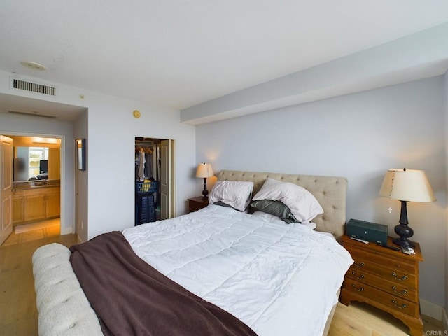 bedroom with light hardwood / wood-style flooring, ensuite bath, and a closet