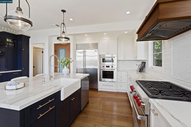 kitchen featuring premium range hood, sink, hanging light fixtures, high end appliances, and a center island with sink