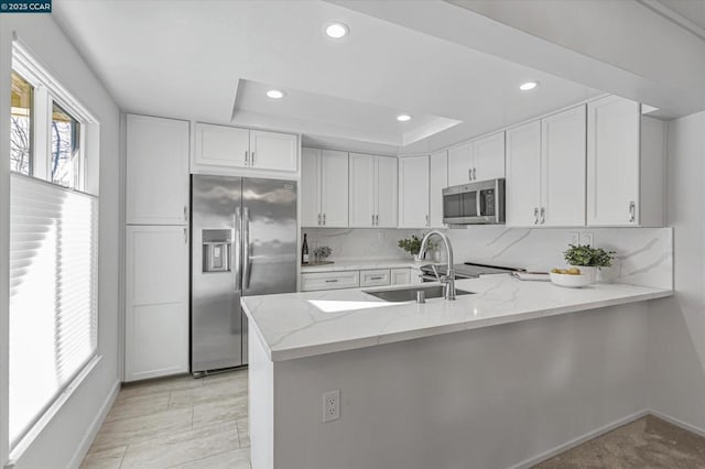 kitchen with stainless steel appliances, kitchen peninsula, light stone countertops, and white cabinets