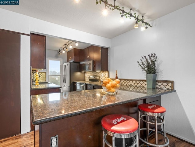 kitchen with appliances with stainless steel finishes, backsplash, light hardwood / wood-style floors, and kitchen peninsula