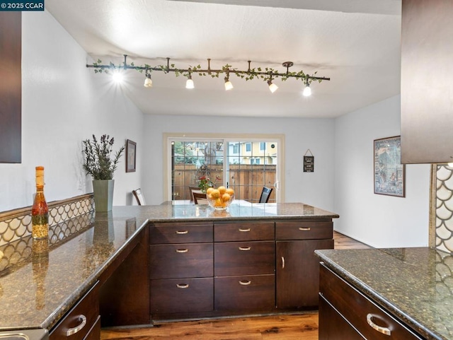 kitchen featuring rail lighting, dark stone countertops, dark brown cabinets, kitchen peninsula, and light wood-type flooring