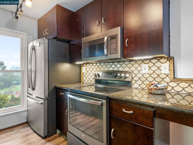 kitchen with light hardwood / wood-style flooring, appliances with stainless steel finishes, dark stone countertops, backsplash, and dark brown cabinetry