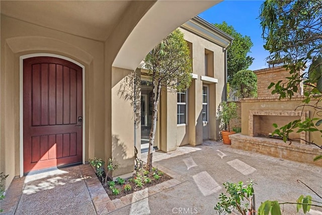 doorway to property with stucco siding, a patio, and an outdoor brick fireplace