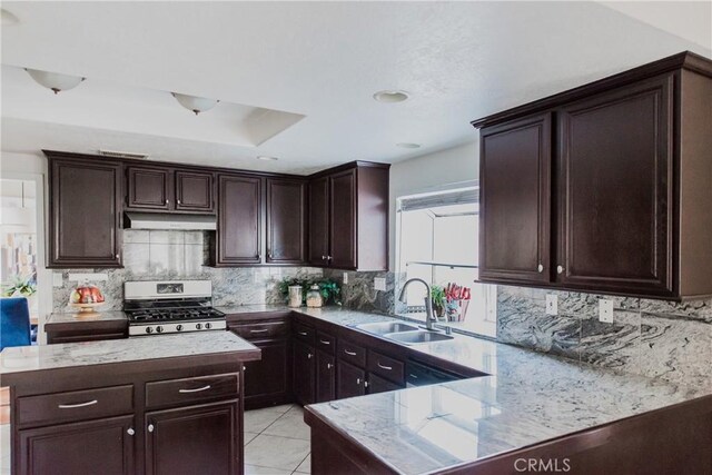 kitchen with dark brown cabinetry, sink, stainless steel range, and light tile patterned floors