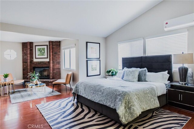 bedroom with multiple windows, a brick fireplace, hardwood / wood-style flooring, and a wall mounted AC