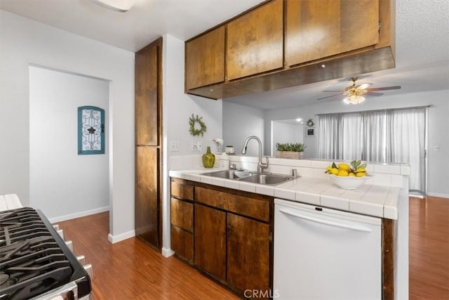 kitchen with sink, dishwasher, stainless steel range with gas stovetop, dark hardwood / wood-style flooring, and tile countertops