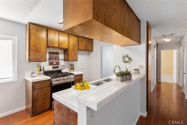 kitchen with sink, light hardwood / wood-style flooring, stainless steel range with gas cooktop, tile counters, and kitchen peninsula