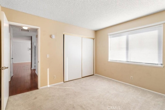 unfurnished bedroom with light carpet, a textured ceiling, and a closet