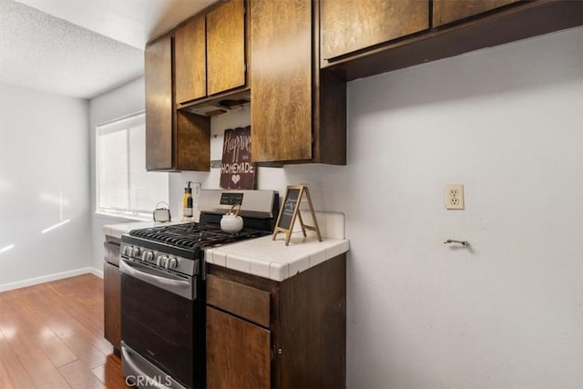 kitchen featuring tile countertops, light hardwood / wood-style floors, a textured ceiling, and stainless steel gas range oven