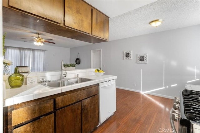 kitchen with sink, white dishwasher, a textured ceiling, dark hardwood / wood-style flooring, and tile countertops