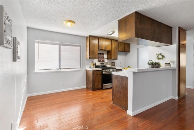 kitchen with hardwood / wood-style floors, gas range, kitchen peninsula, and a textured ceiling