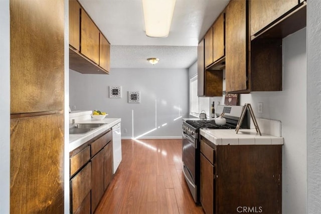 kitchen featuring wood-type flooring, sink, fridge, white dishwasher, and stainless steel gas range oven