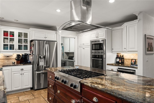 kitchen featuring white cabinets, backsplash, island exhaust hood, washing machine and clothes dryer, and stainless steel appliances