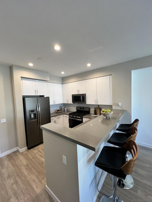 kitchen with a breakfast bar, appliances with stainless steel finishes, kitchen peninsula, light hardwood / wood-style floors, and white cabinets