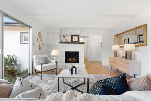 living room featuring beamed ceiling, plenty of natural light, a brick fireplace, and light hardwood / wood-style flooring