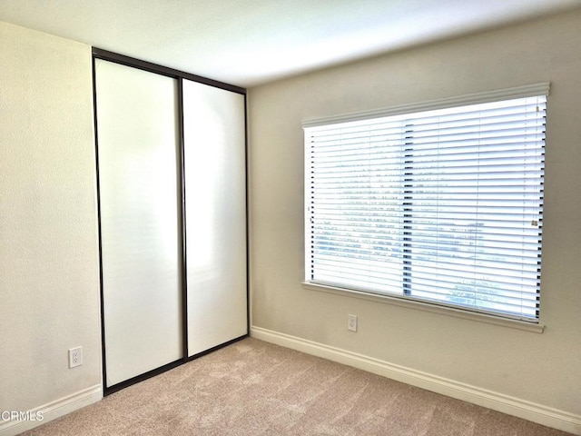 unfurnished bedroom with multiple windows, light carpet, and a closet