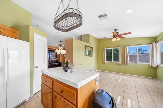 kitchen featuring a kitchen island, light tile patterned flooring, white refrigerator with ice dispenser, and tile countertops