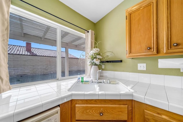 kitchen featuring tile counters, dishwashing machine, and sink