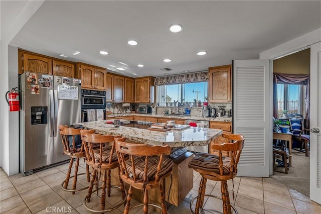 kitchen featuring light stone counters, a center island, light tile patterned floors, appliances with stainless steel finishes, and a kitchen breakfast bar