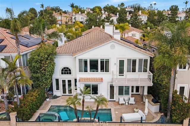 rear view of property featuring a patio area, french doors, a balcony, and an in ground hot tub