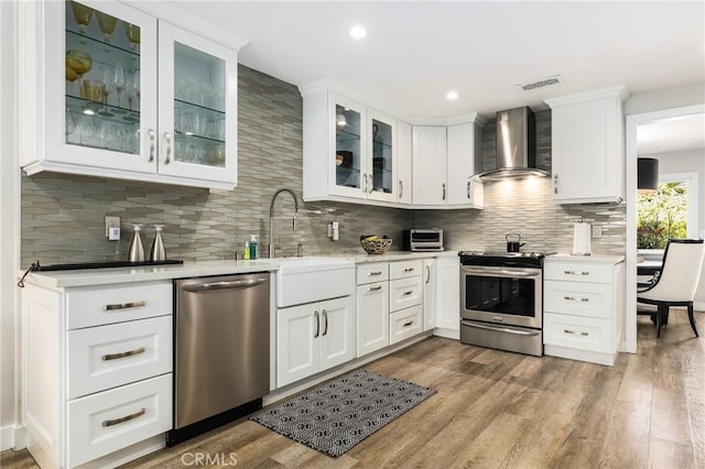 kitchen featuring sink, white cabinetry, hardwood / wood-style flooring, stainless steel appliances, and wall chimney range hood