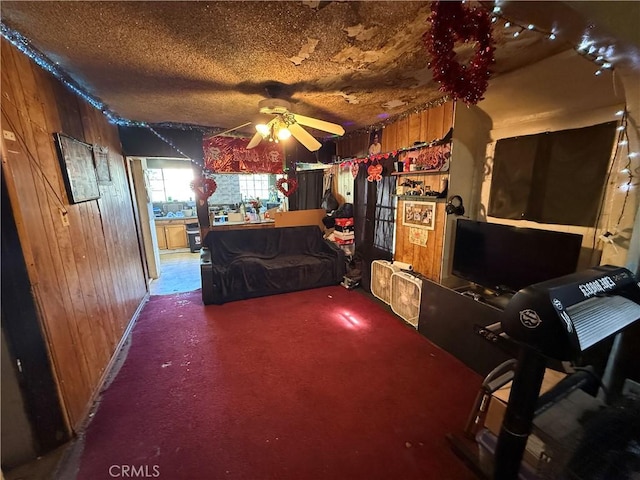 interior space with ceiling fan, wooden walls, carpet, and a textured ceiling