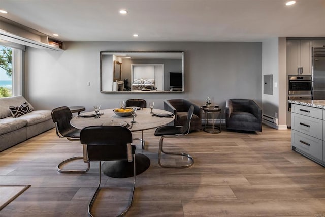 living room with baseboard heating, electric panel, and light hardwood / wood-style flooring