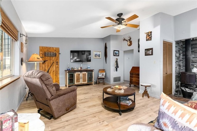 living room with ceiling fan, plenty of natural light, a wood stove, and light wood-type flooring