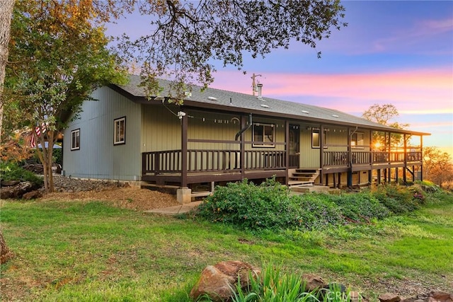 back house at dusk featuring a wooden deck and a yard