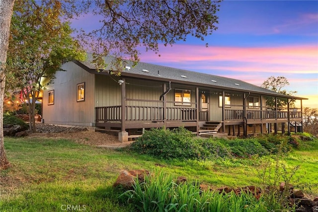 back house at dusk featuring a deck and a lawn