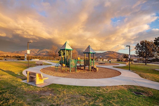 playground at dusk featuring a mountain view and a yard