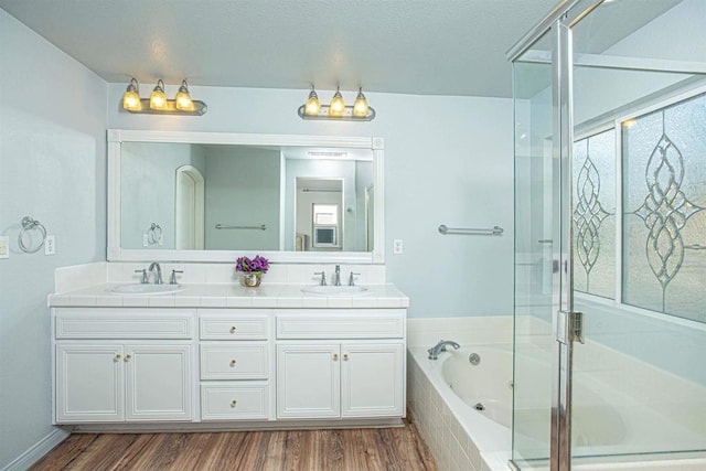 full bath with a garden tub, double vanity, wood finished floors, and a sink