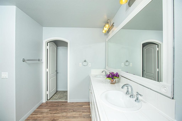 full bathroom with double vanity, a sink, baseboards, and wood finished floors